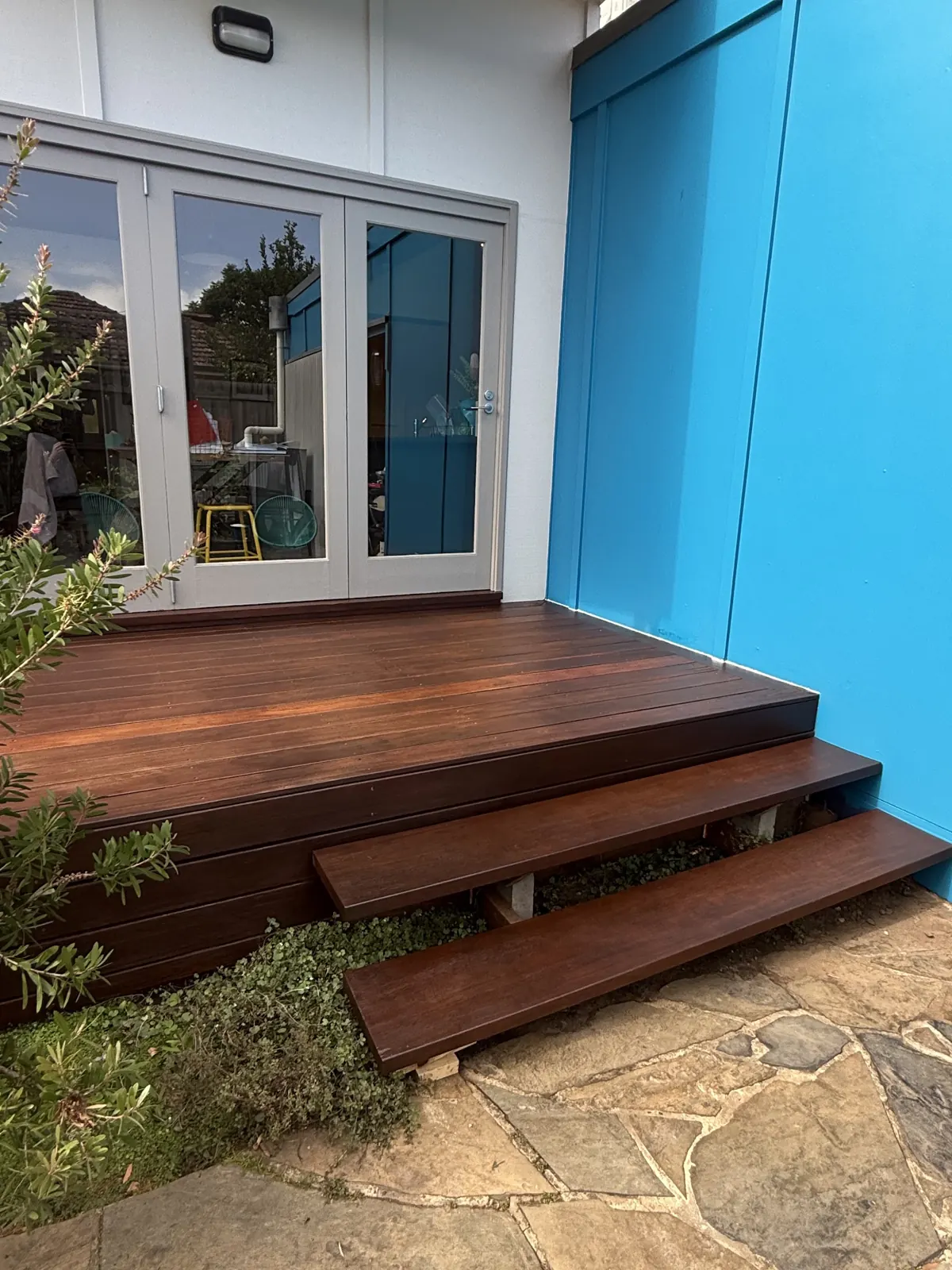Rich red-brown merbau deck with two floating steps down to crazy paving